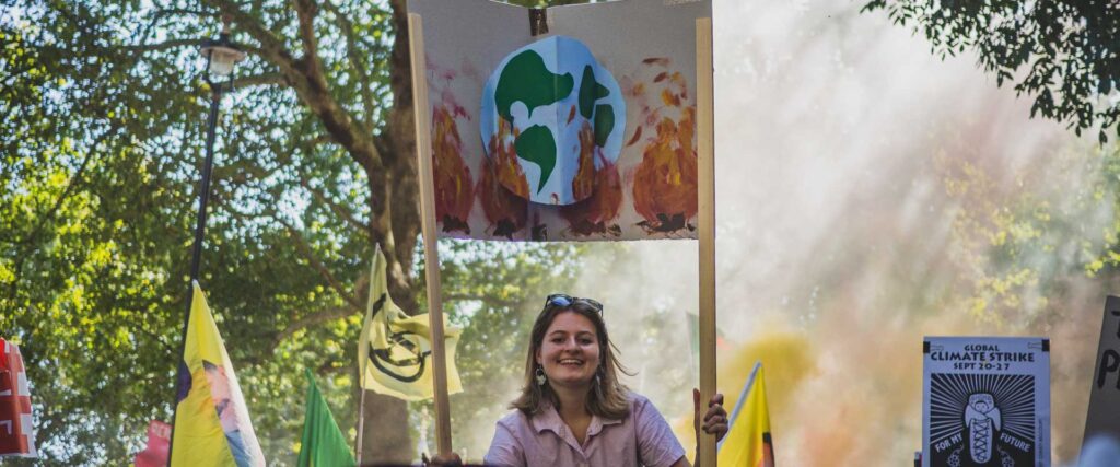 Photo of a young woman, holding a sign showing the earth on fire, at a climate demonstration. Credit Gabriel Mccallin.