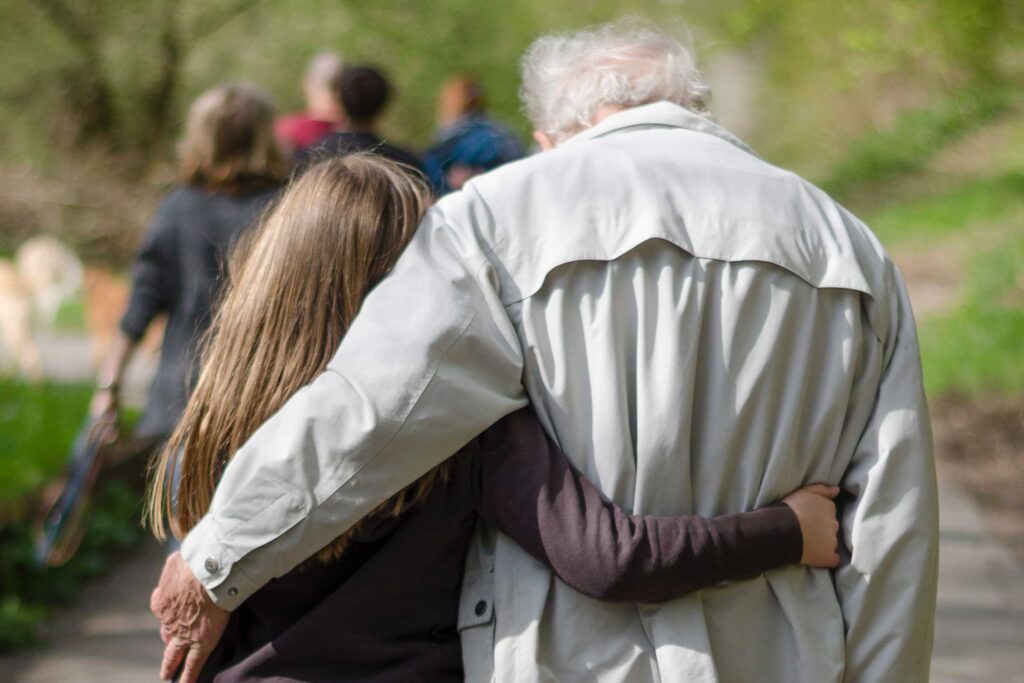 A photo of a young woman and old man, from behind, with their arms around each other. Credit Jana Sabeth.