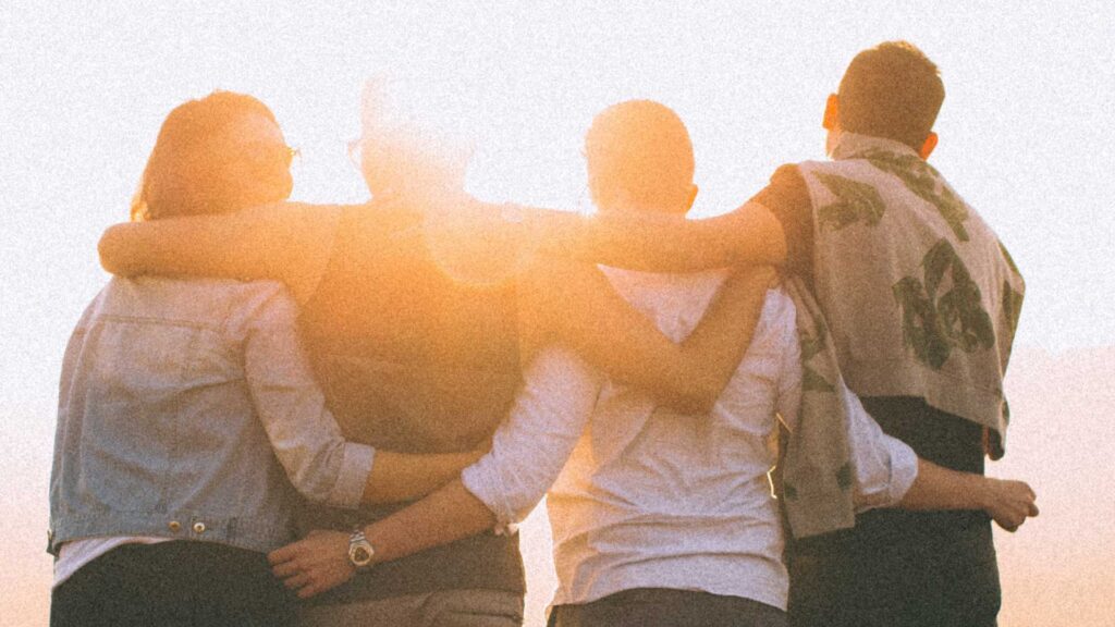 Photo of four youth, arms around each other, looking towards a sunrise. Credit Helena Lopes.