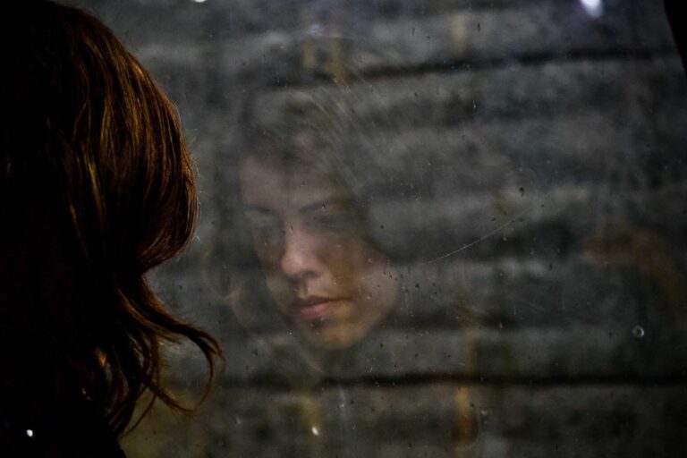 A photo of a young woman's reflection in a window. Photo by Tiago Bandeira.