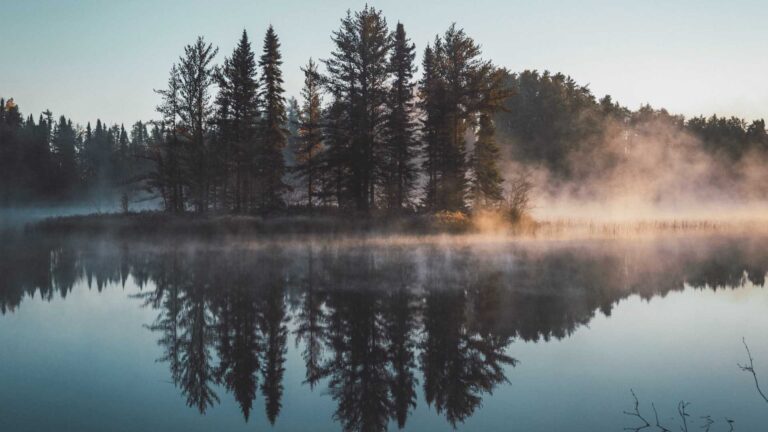 Photo of an island in a lake with mist rising from the water. Photo by Juan Davila on Unsplash