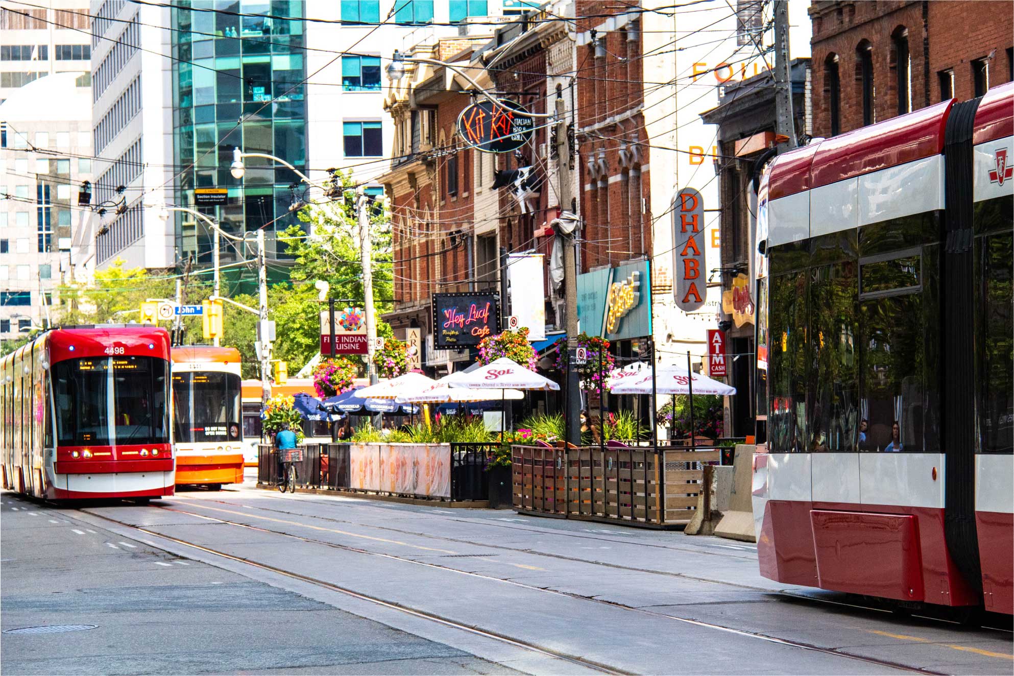 A photo of streetcars in Toronto, Ontario. Restaurants are in the background, with patio seating on the sidewalk. Photo by Debora Fontana on Unsplash