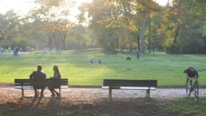 Photo of an urban park, with benches on which people are sitting in the foreground and lawn and trees in the background. Photo by I Do Nothing But Love on Unsplash .