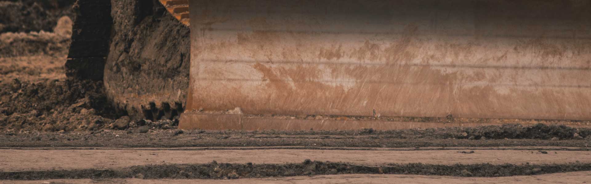 Closer up photo of a bulldozer blade resting on scraped bare dirt. Credit Jason Jarrach.
