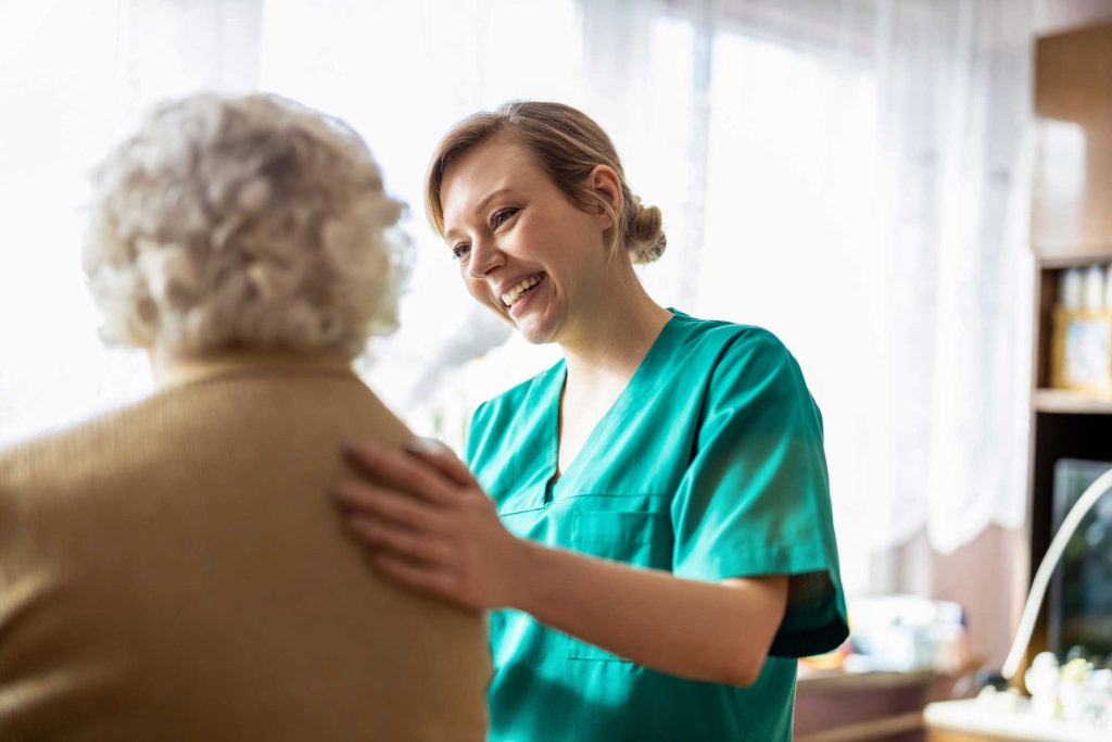 Photo of a woman, possibly a doctor, in green scrubs, patting the back of an elderly woman.