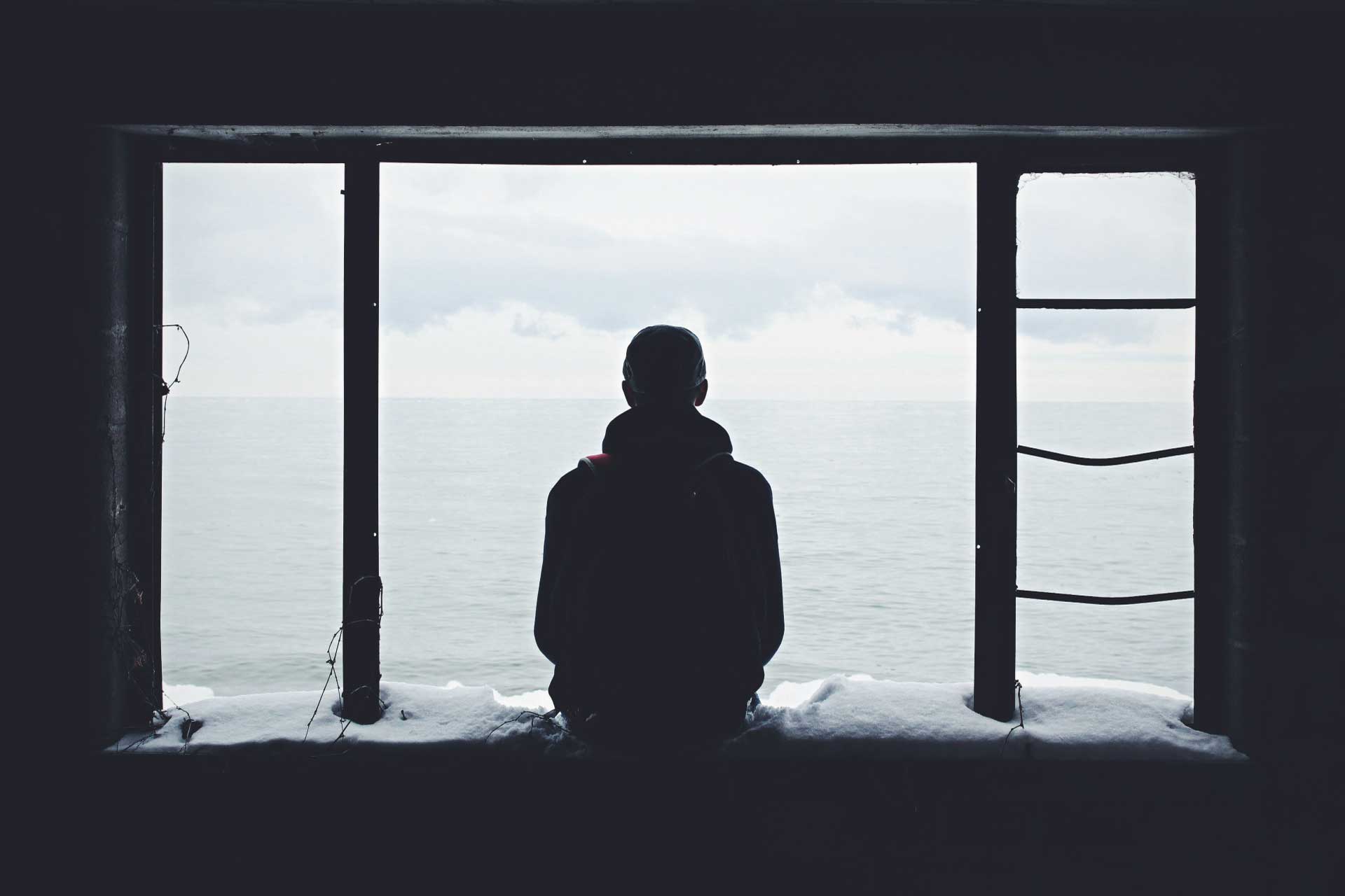 Photo of a person's back, sitting in an empty window, silhouetted against water. Credit Noah Silliman.